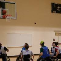 Group of adults in wheelchairs underneath basketball hoop with the ball near the rim.